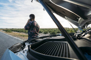 Man talking on mobile phone by breakdown car at roadside - DAMF00909