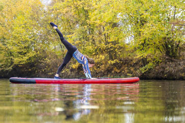 Sportswoman practicing yoga on paddleboard at Rems river, Baden-Wurttemberg, Germany - STSF03105