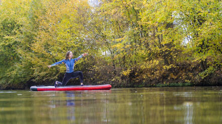 Young athlete practicing yoga pose on paddleboard at Rems river, Baden-Wurttemberg, Germany - STSF03106