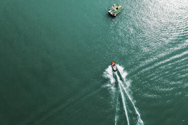Luftaufnahme eines Motorboots, das seine Spur über den türkisfarbenen Wörthersee zieht - DAWF02217