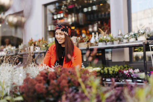 Smiling woman looking at flowers on retail display - DAWF02221