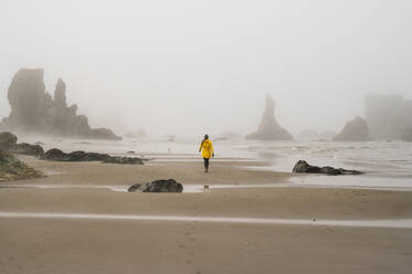 Girl in yellow rain jacket walking on foggy oregon beach - CAVF95121