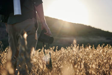 Nahaufnahme eines Fotografen, der eine Kamera auf einer Wiese bei Sonnenuntergang hält - CAVF95162
