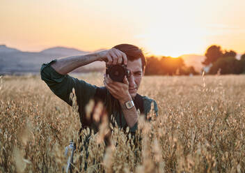 Porträt eines Fotografen mit Blick auf die Kamera auf einer Wiese bei Sonnenuntergang - CAVF95163