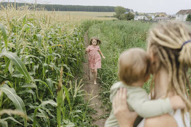 Girl running towards mother carrying toddler son in corn field - SEAF00068