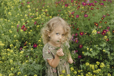 Girl holding plant standing amidst flowering plants - SEAF00076
