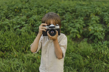 Boy photographing through vintage camera on field - SEAF00085