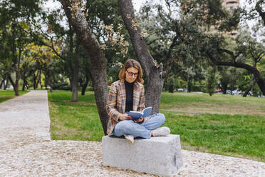 Freelancer reading book on bench at park - MRRF01682