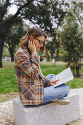 Freelancer reading book on bench in public park - MRRF01684
