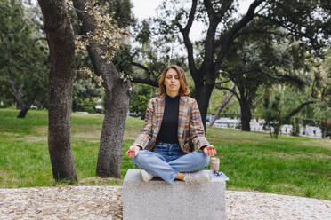 Geschäftsfrau meditiert auf einer Bank in einem öffentlichen Park - MRRF01685
