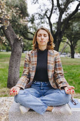 Freelancer meditating on bench at public park - MRRF01686