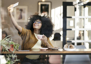 Smiling woman taking selfie through mobile phone in cafe - JCCMF04527