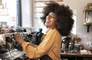 Kellnerin mit Afrofrisur an der Kaffeemaschine im Café - JCCMF04543