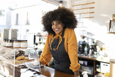 Kellnerin mit Afrofrisur lehnt sich an den Tresen eines Cafés - JCCMF04544