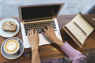 Businesswoman with coffee cup and pastry using laptop on cafe table - JCCMF04549