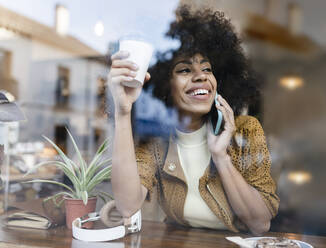 Smiling woman with coffee up talking on mobile phone in cafe - JCCMF04560