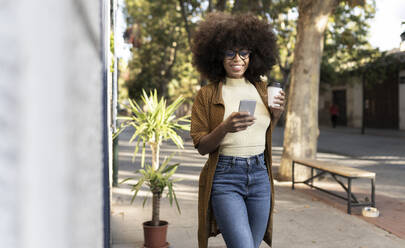 Smiling woman with disposable coffee cup using mobile phone on footpath - JCCMF04561