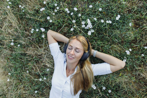 Schöne Frau mit drahtlosen Kopfhörern, die sich im Gras entspannt - TYF00041
