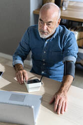 Älterer Mann mit Blutdruckmessgerät bei Videogespräch mit Arzt über Laptop - GIOF14122