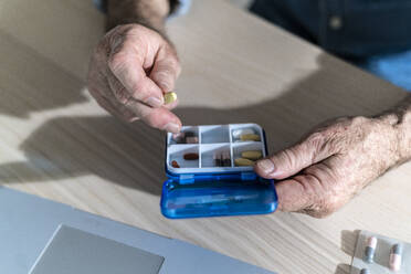 Hands of senior man taking out medicine from pill box at dining table - GIOF14134