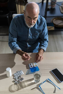 Älterer Mann nimmt am Esstisch Medikamente ein - GIOF14139