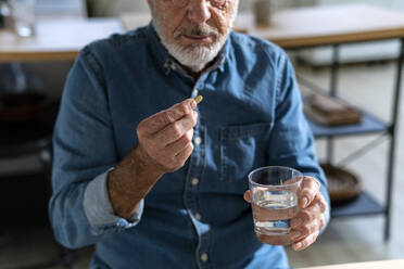 Senior man holding glass of water taking medicine at home - GIOF14140