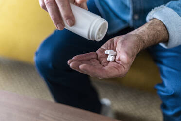 Man removing medicine from container at home - GIOF14141