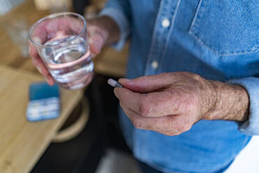 Mann hält ein Glas Wasser und eine Kapsel zu Hause - GIOF14145