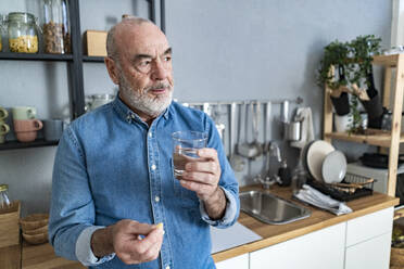 Nachdenklicher älterer Mann nimmt zu Hause in der Küche Medikamente ein - GIOF14150