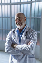 Happy senior doctor in lab coat standing with arms crossed - GIOF14153