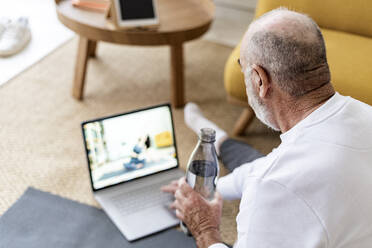 Mann sieht sich zu Hause auf dem Laptop einen Online-Yoga-Kurs an - GIOF14188