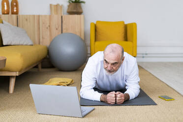 Mann lernt die Plank-Pose mit Hilfe eines Laptops zu Hause - GIOF14189