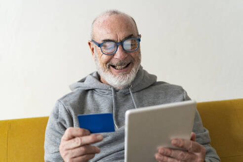 Bearded senior man doing online shopping through tablet PC at home - GIOF14202