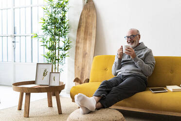 Lächelnder älterer Mann trinkt Kaffee auf dem Sofa - GIOF14207