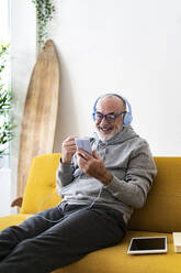 Mann mit Kopfhörern führt zu Hause Videogespräche über sein Mobiltelefon - GIOF14211