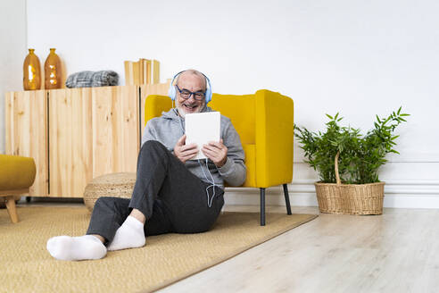 Glücklicher Mann, der an einem Videoanruf über einen Tablet-PC im Wohnzimmer teilnimmt - GIOF14213