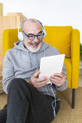 Lächelnder Mann mit Kopfhörern, der während eines Videoanrufs über einen Tablet-PC zu Hause spricht - GIOF14214