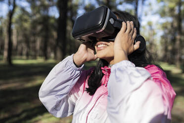Frau schaut durch ein Virtual-Reality-Headset im Park an einem sonnigen Tag - JCCMF04567