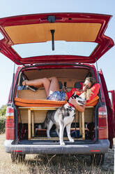 Frau auf Autoreise entspannt sich im Kofferraum des Vans und umarmt ihren Hund - JCMF02239