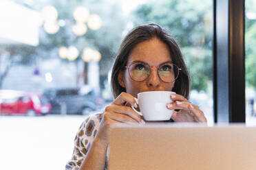 Geschäftsfrau mit Brille trinkt Kaffee in einem Cafe - PNAF02543