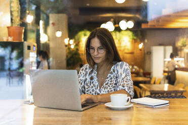 Junger Freiberufler arbeitet am Laptop in einem Café - PNAF02550