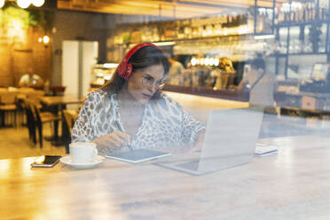Junger Freiberufler arbeitet mit Grafiktablett und Laptop in einem Café - PNAF02555