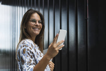 Smiling businesswoman with mobile phone looking away - PNAF02566