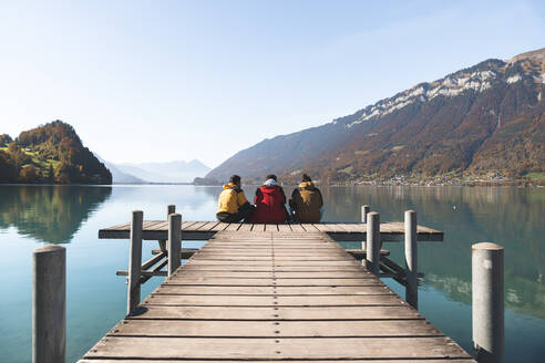 Freunde sitzen auf dem Steg und schauen auf die Berge in Interlaken, Schweiz - JAQF00913