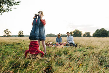 Siblings playing in park with parents in background - ASGF01680