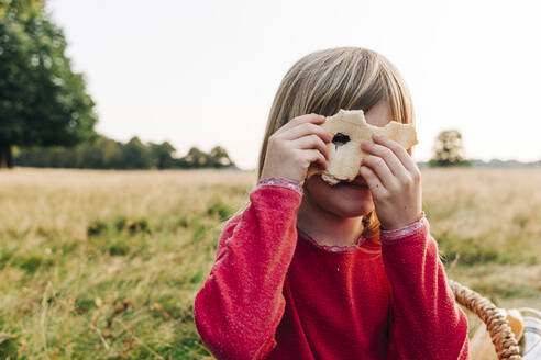 Cute girl looking through hole on bread in park - ASGF01685