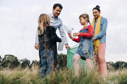 Daughters collecting plastic bottle with parents in park - ASGF01696