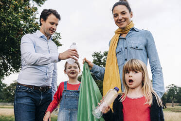 Töchter sammeln mit Eltern Plastikflaschen im Park - ASGF01703