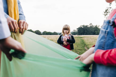 Girl collecting plastic bottles with family in park - ASGF01704