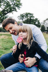 Vater sieht seine Tochter an, die im Park einen Lutscher isst - ASGF01715